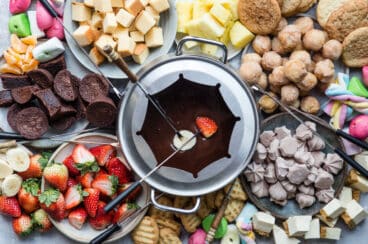 A platter of chocolate fondue and colorful dippers like fruit and sweets.