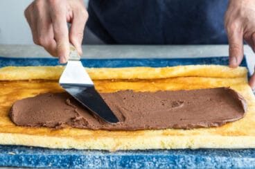 Chocolate frosting being spread over a roll cake.