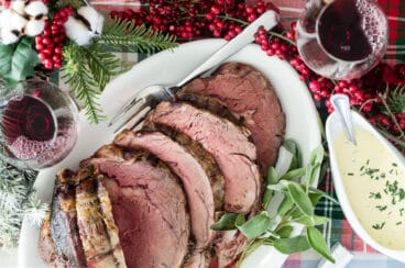 Prime rib cut into slices on a white platter with a serving fork.