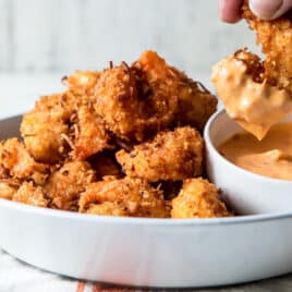 Someone dipping coconut shrimp in sauce.