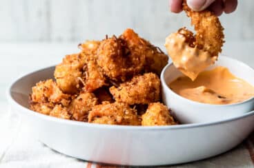 Someone dipping coconut shrimp in sauce.