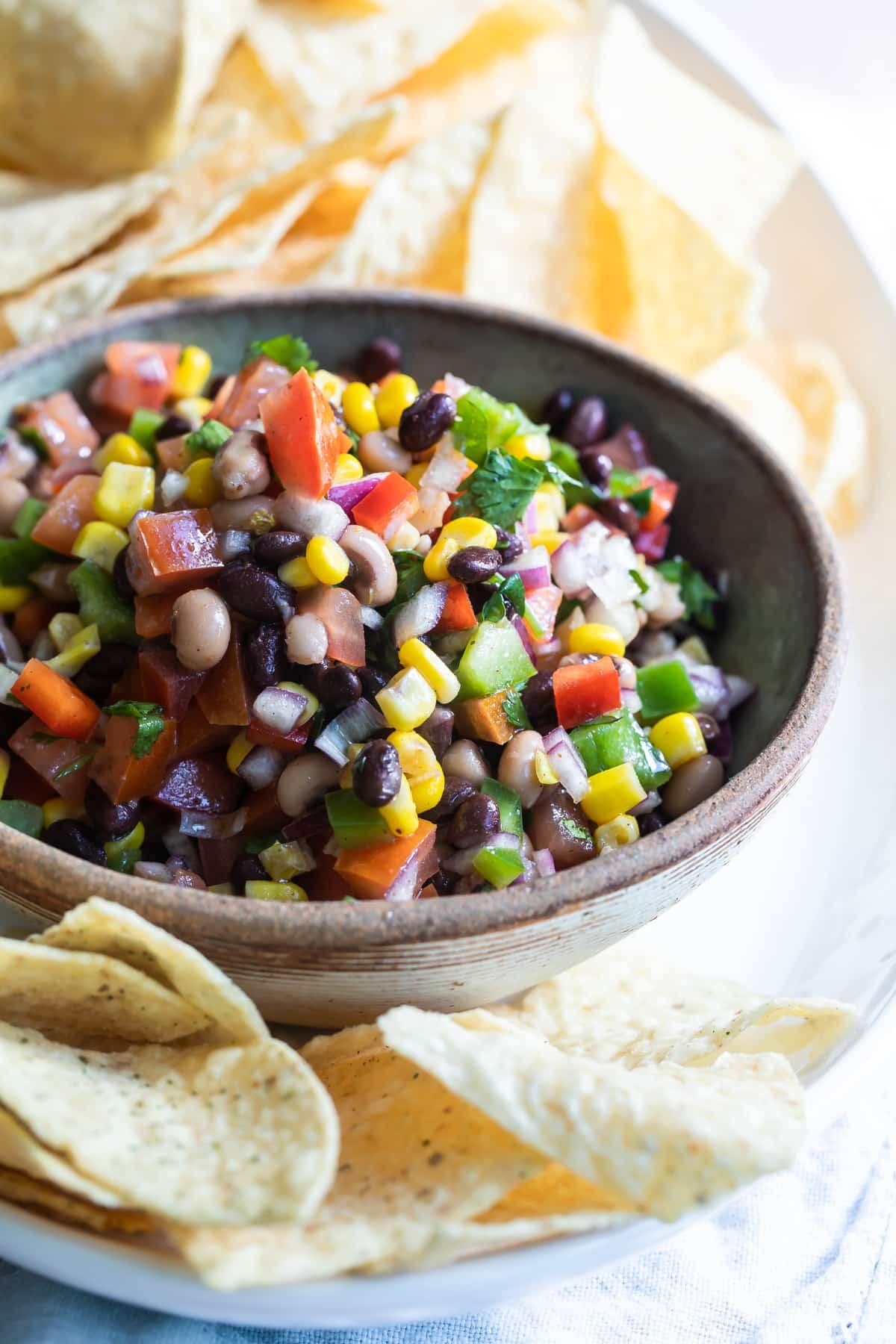 Cowboy caviar in a bowl on a white plate with tortilla chips.