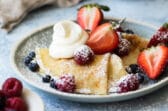 A plate of crepes with whipped cream and berries on top.