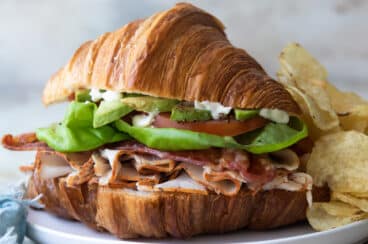 A croissant sandwich on a plate with potato chips.
