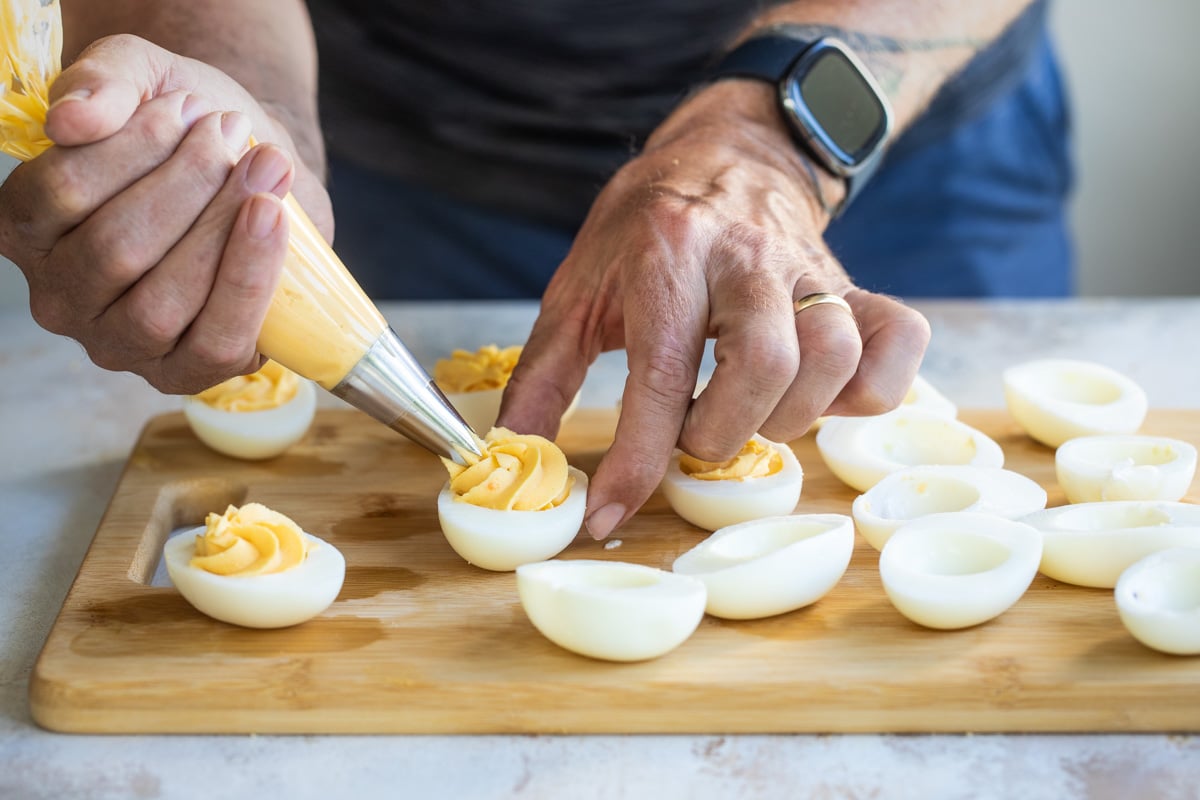 Someone filling hard boiled egg white halves with yellow yolk filling.