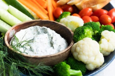 A platter with dill dip and fresh vegetables.