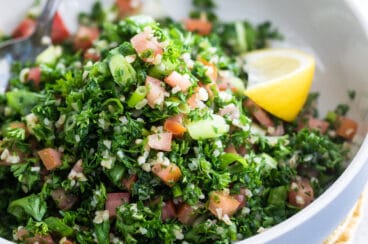Bulgar tabbouleh in a white bowl with a lemon garnish.