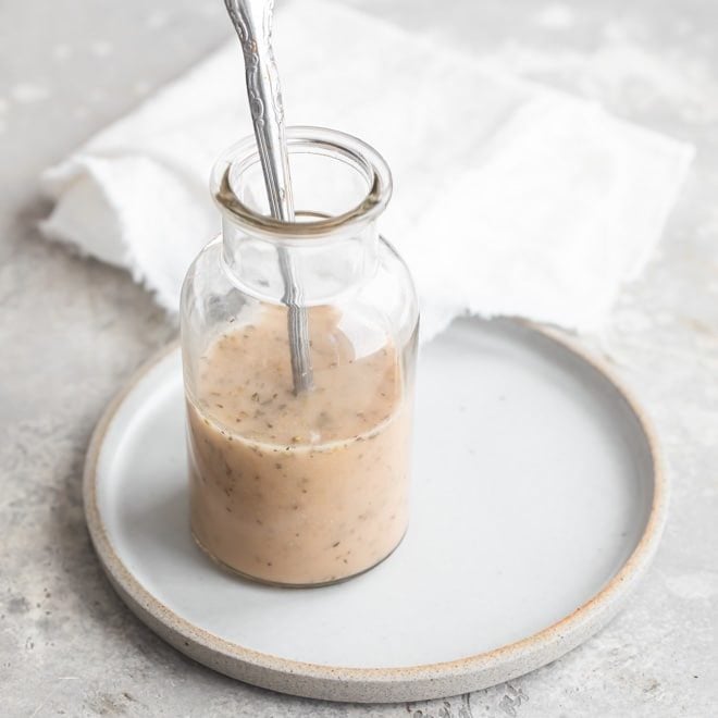 Easy cold pasta salad dressing in a clear jar on a white plate with a spoon.