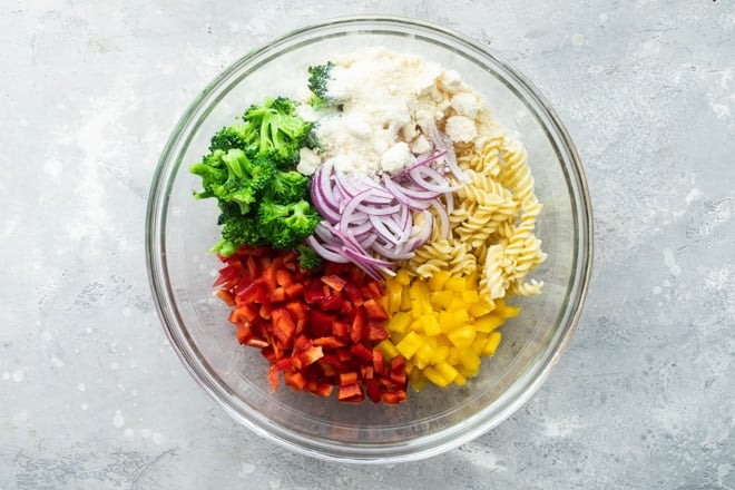 Separated easy cold pasta salad ingredients in a clear bowl.