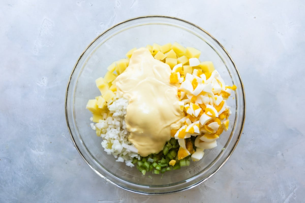 Ingredients for potato salad in a clear bowl before being mixed.