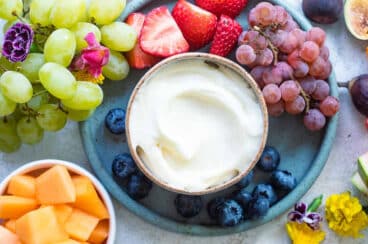 A small brown bowl of fruit dip surrounded by various fruits.