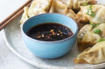 A platter of potstickers, someone holding one with chopsticks.