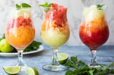 Three granitas on a counter surrounded by garnishes.
