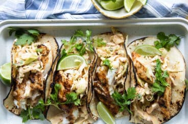 Four grilled fish tacos on a platter.