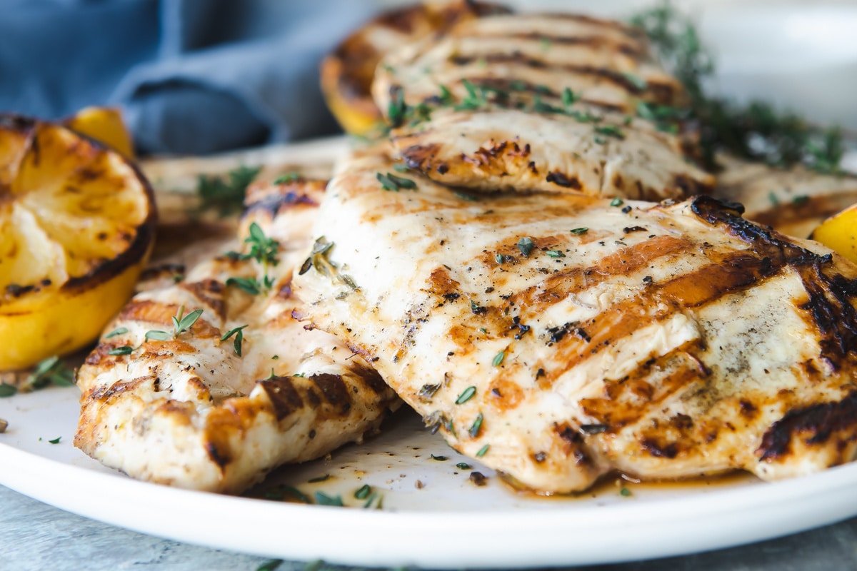 A platter with grilled lemon chicken breasts on it.