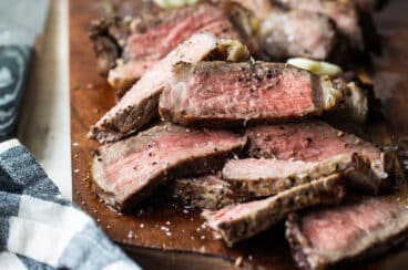 Grilled New York strip slices on a wooden cutting board.