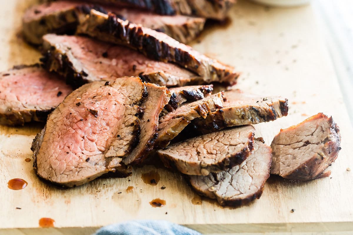 A cutting board with a sliced tri tip on top.