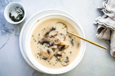 Homemade cream of mushroom soup in a white bowl with a gold spoon.