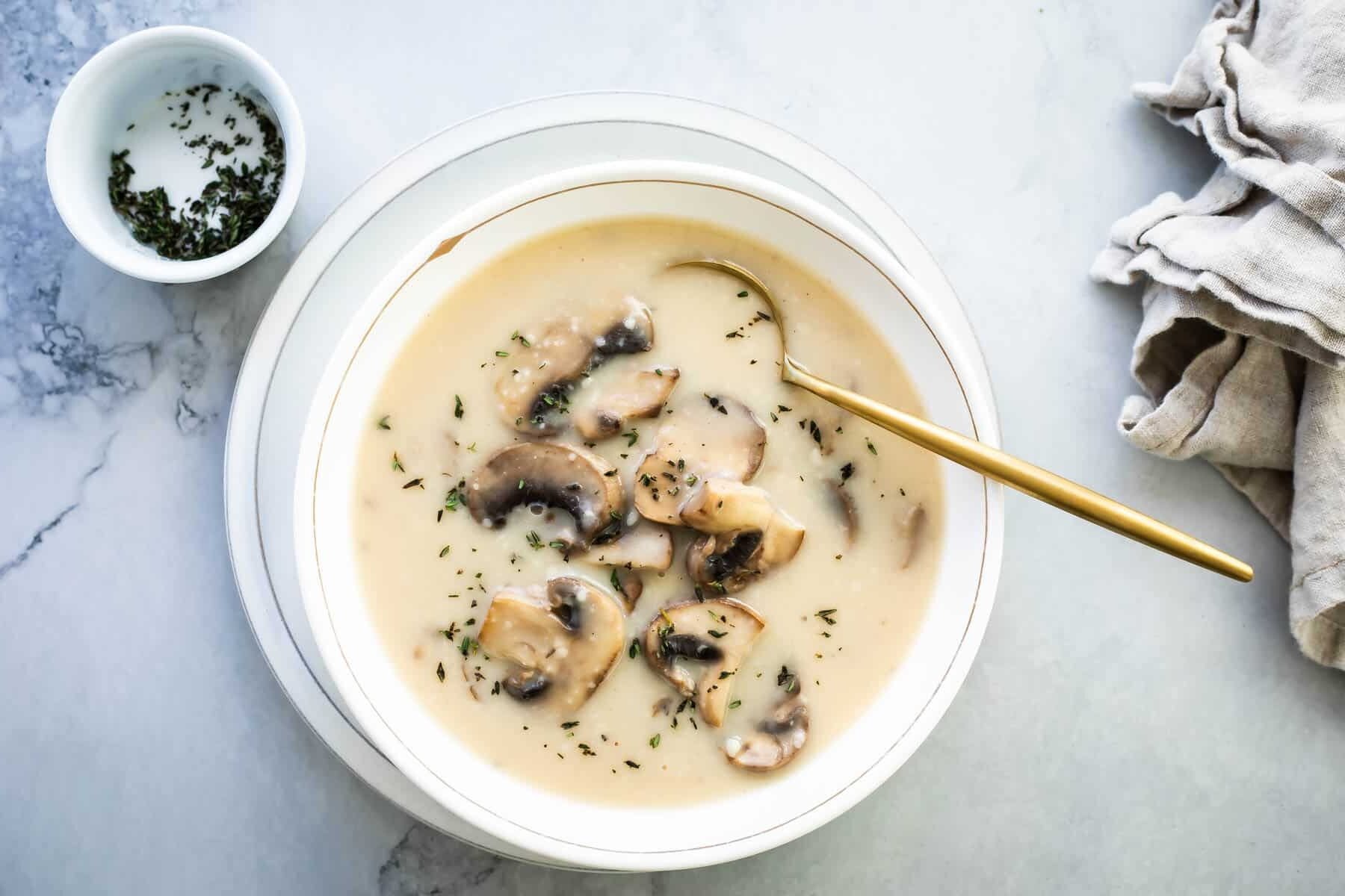 Homemade cream of mushroom soup in a white bowl with a gold spoon.