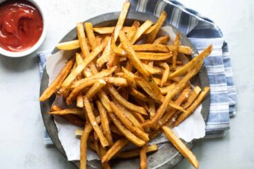 A pile of french fries on a plate next to a cup of ketchup.