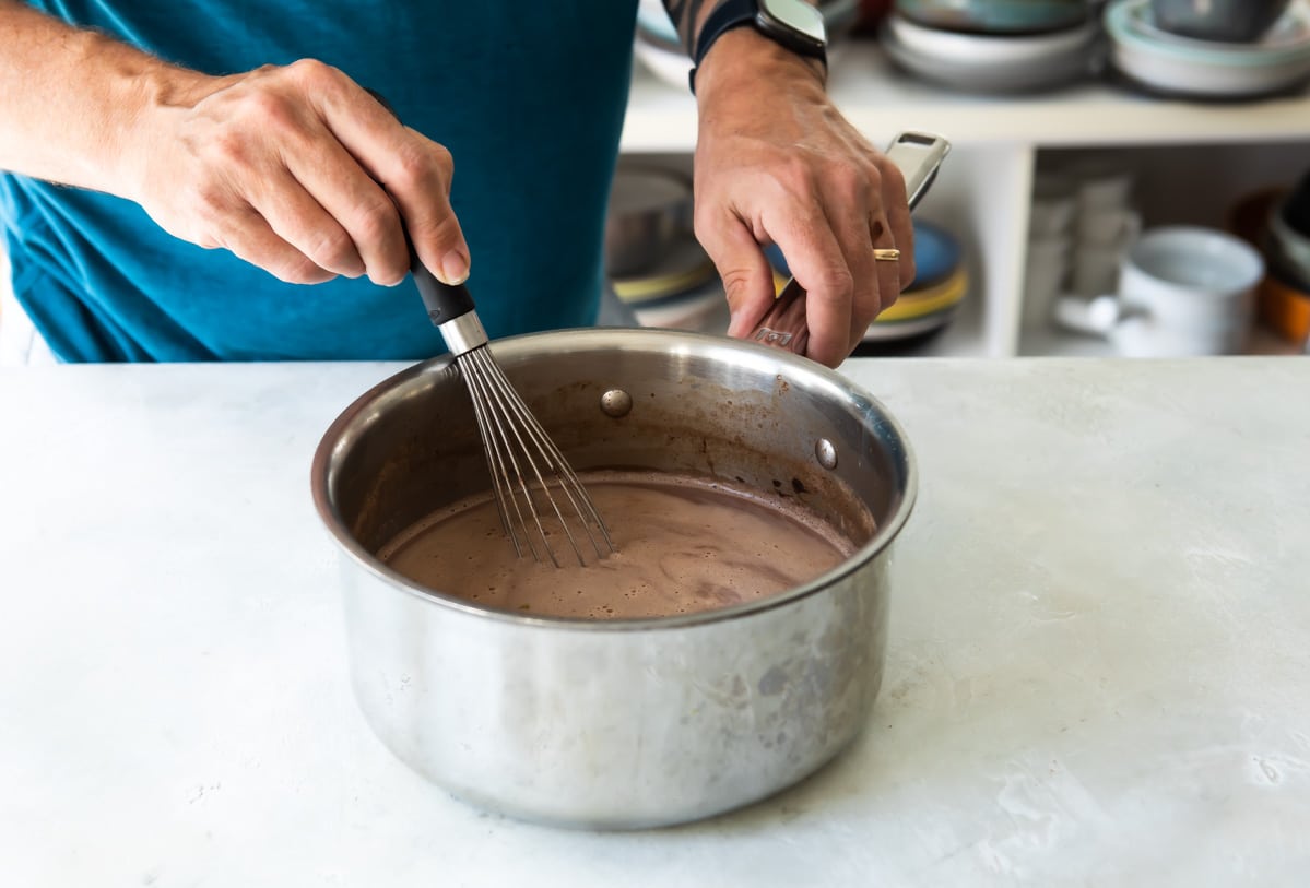Hot chocolate being mixed in a silver saucepan.