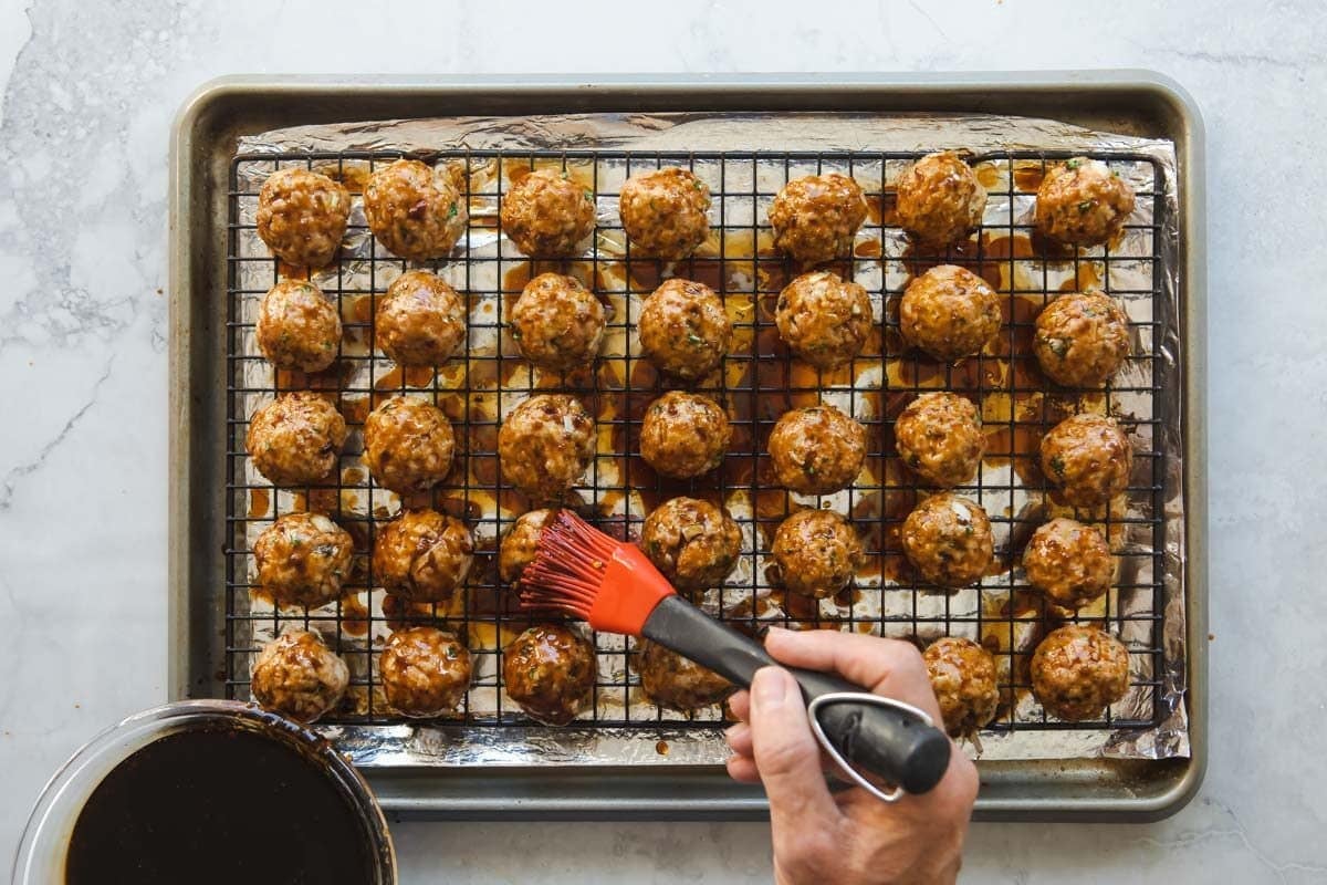 Rows of baked meatballs on a baking rack set over a baking sheet.