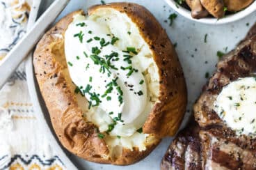 A plate with a baked potato topped with sour cream, a steak topped with butter, and a bowl of balsamic mushrooms on a plate.