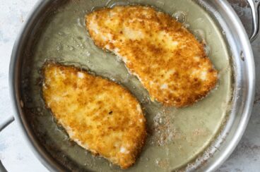 Chicken being breaded in a silver skillet.