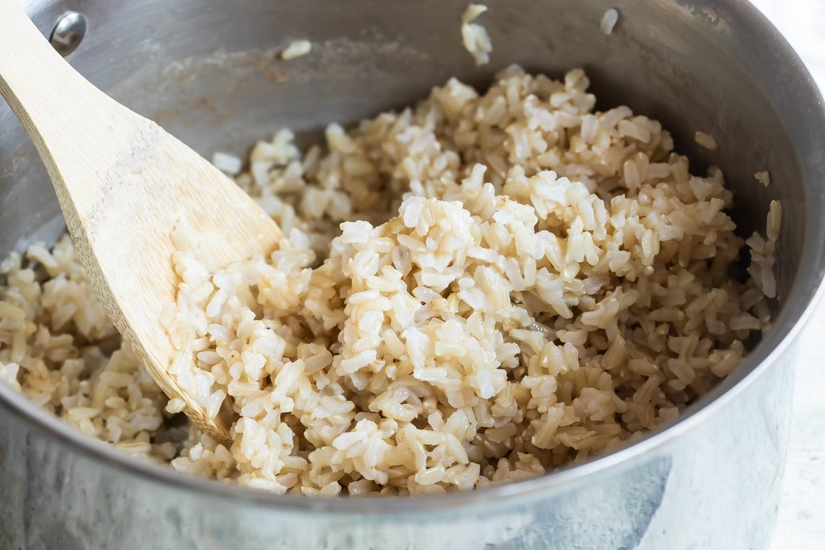A metal saucepan with a spoon and brown rice in it.