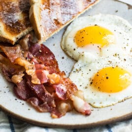 Sunny side up eggs on a plate with bacon and toast.