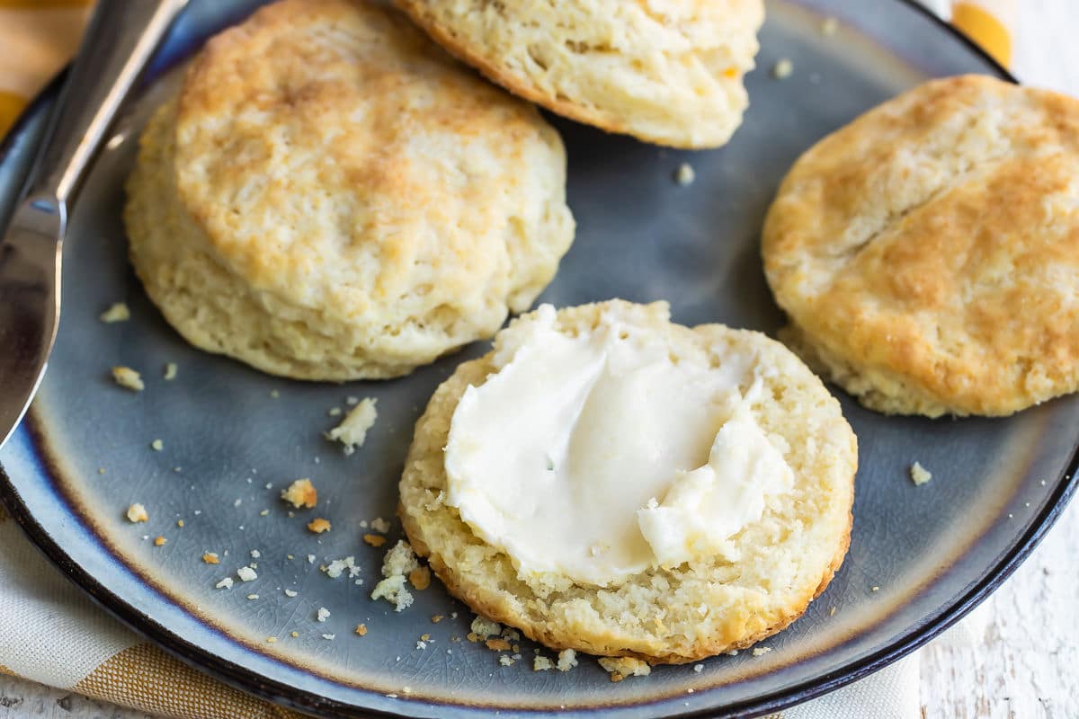 A plate with biscuits cut in half, one piece slathered in butter.