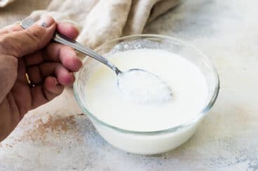 Someone scooping a spoonful of buttermilk out of a small glass bowl.