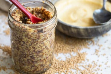A mason jar with mustard and a red spoon in it.