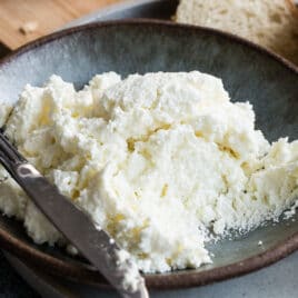 Homemade ricotta cheese in a blue bowl with a knife resting along the side.