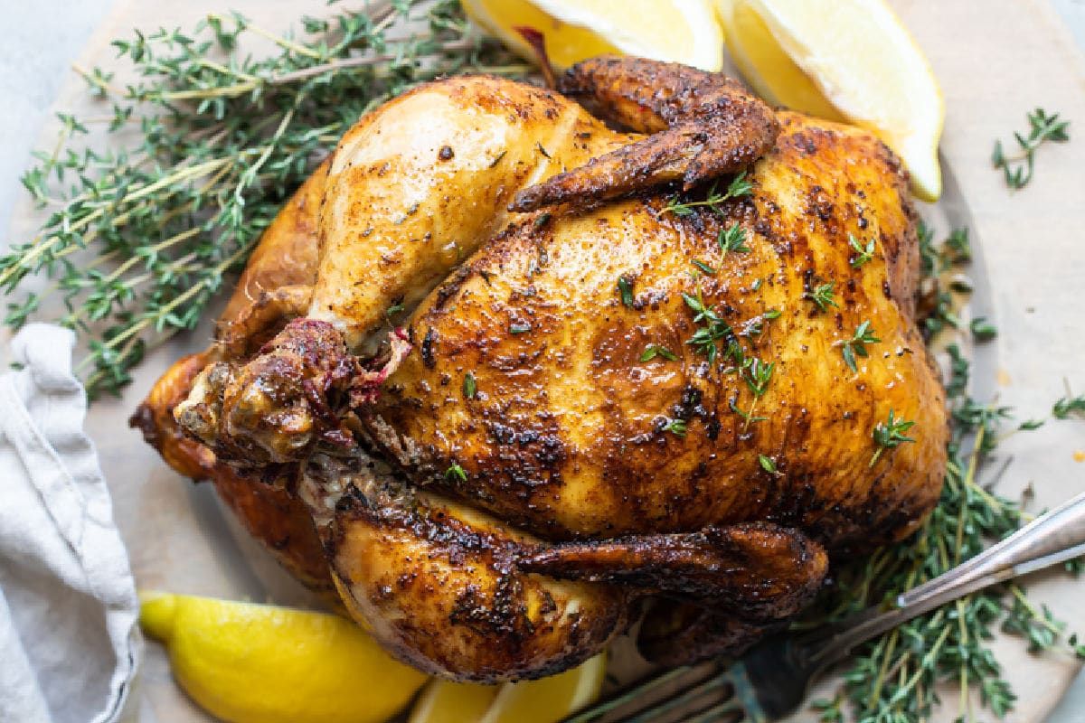 A rotisserie chicken on a white plate with slices of lemon.