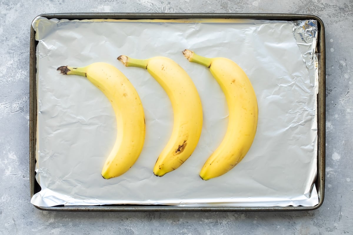 3 unpeeled yellow bananas on a foil-lined baking sheet.