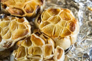 Bulbs of roasted garlic on a piece of crumpled aluminum foil.