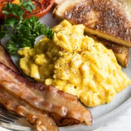 A plate with scrambled eggs, bacon, toast and parsley.