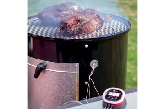 A weber charcoal smoker with meat on top.