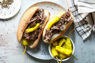Two Italian beef sandwiches on a plate with pepperoncinis.