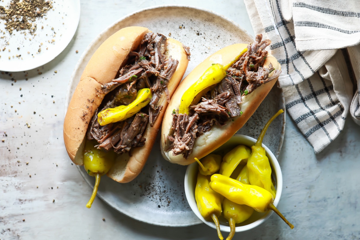 Two Italian beef sandwiches on a plate with pepperoncinis.
