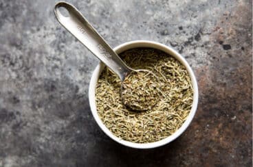 A small bowl filled with Italian seasoning and a measuring spoon.