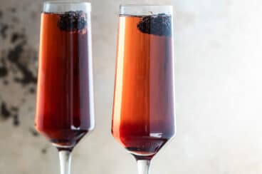 Two Kir Royale cocktails in champagne flutes on a metal tray.