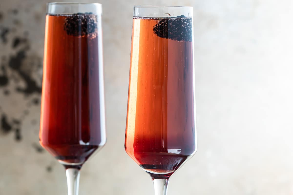 Two Kir Royale cocktails in champagne flutes on a metal tray.