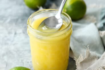 A jar of lime curd with a spoon scooping some out.