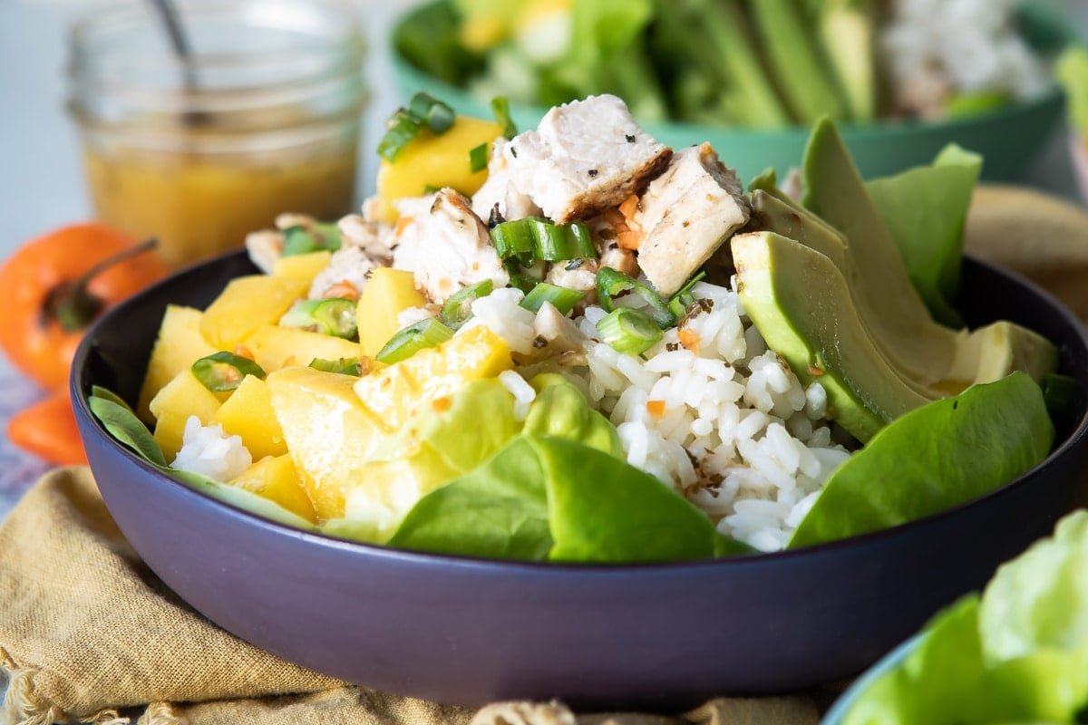 A black bowl with filled with a mango, chicken rice combination.