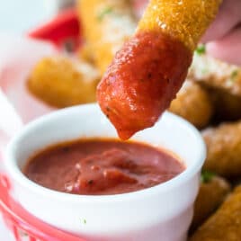 Marinara dipping sauce with mozzarella sticks in a red basket.