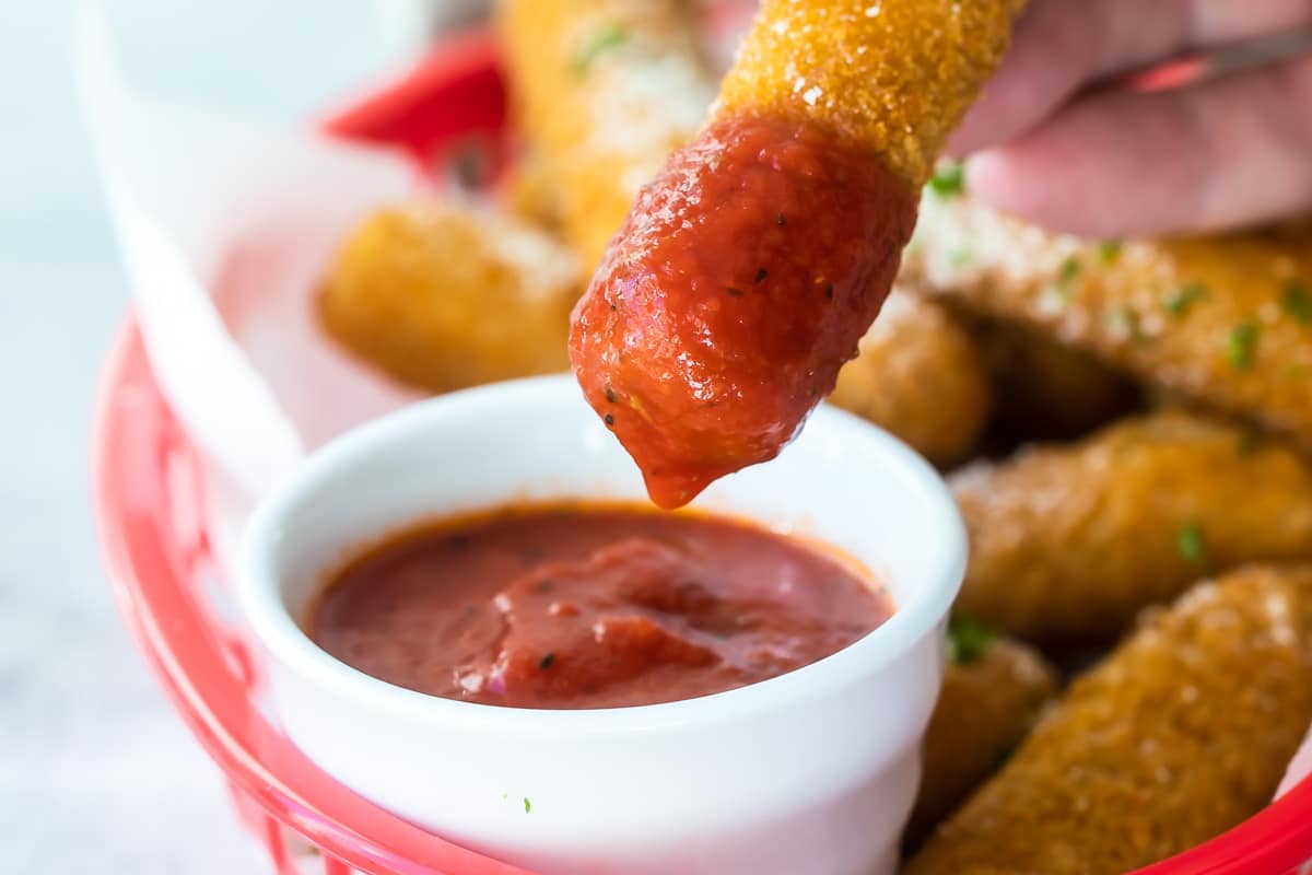 Marinara dipping sauce with mozzarella sticks in a red basket.