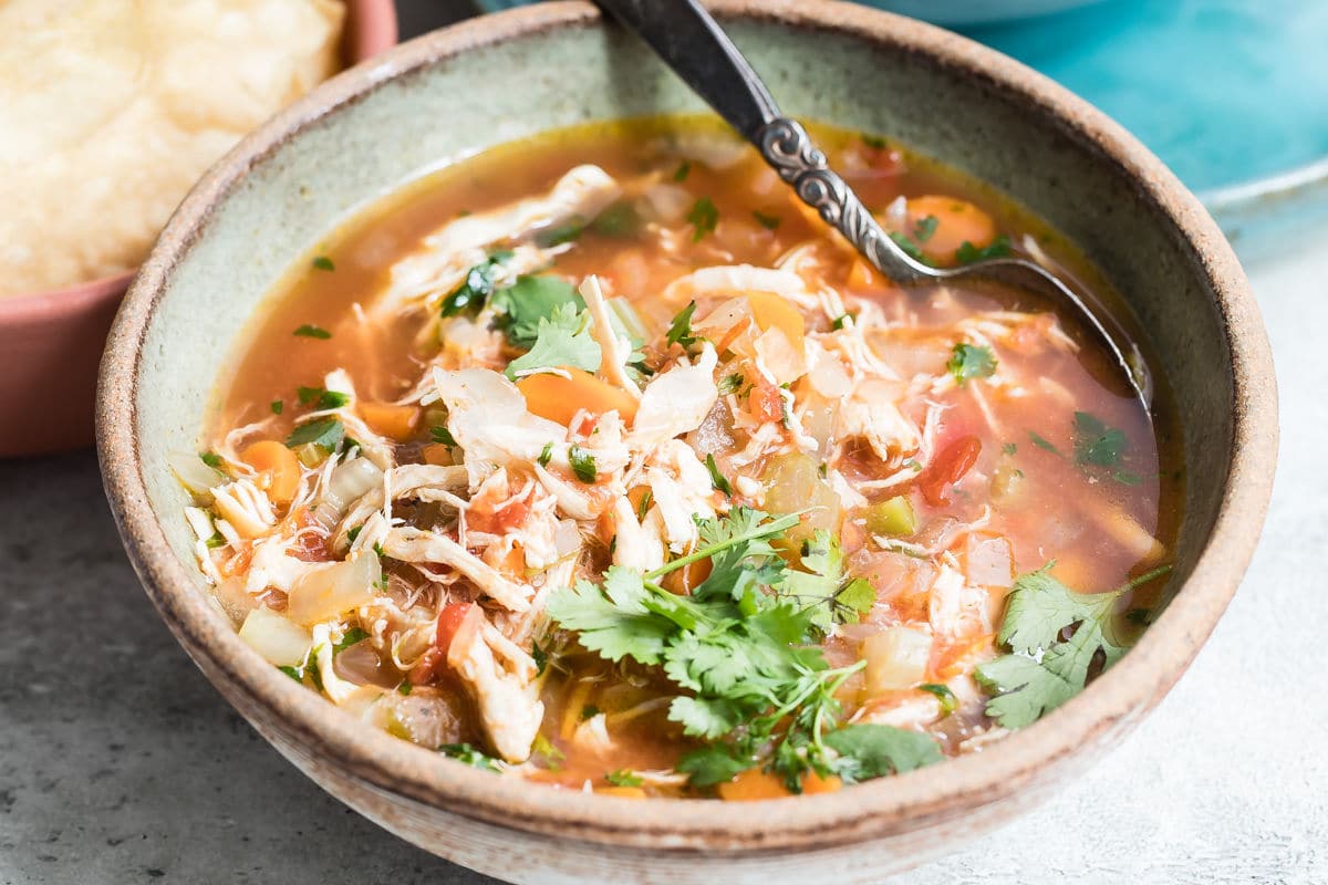 One bowl of Mexican chicken soup with toppings nearby.