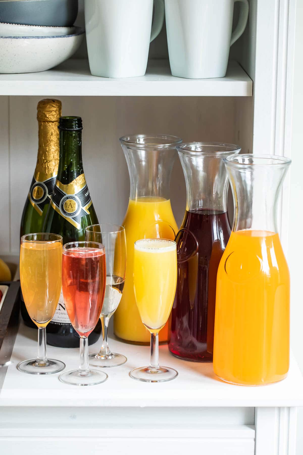 Carafes of juice, bottles of sparkling wine, and fresh fruit garnishes for a mimosa bar.